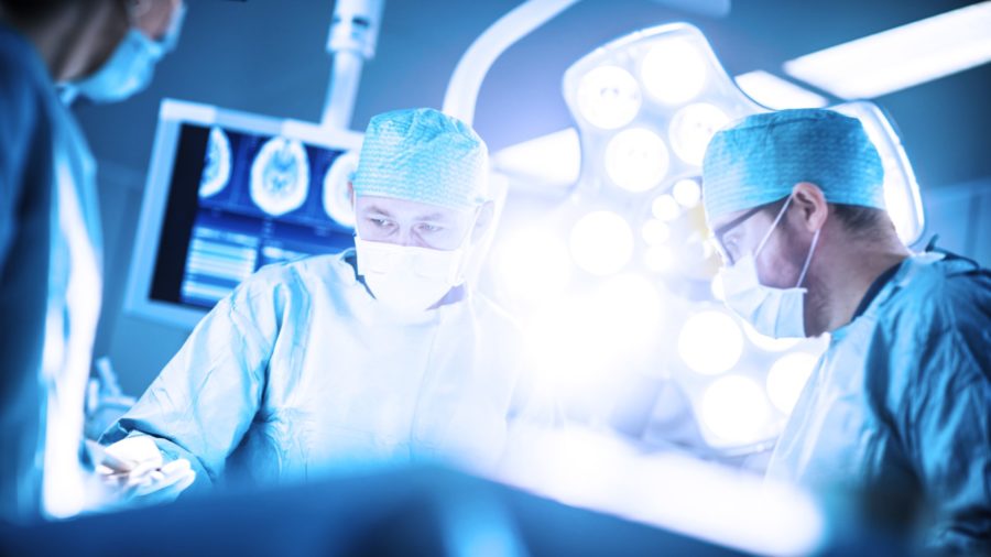 Low Angle Shot in the Operating Room, Assistant Hands out Instruments to Surgeons During Operation. Surgeons Perform Operation. Professional Medical Doctors Performing Surgery.